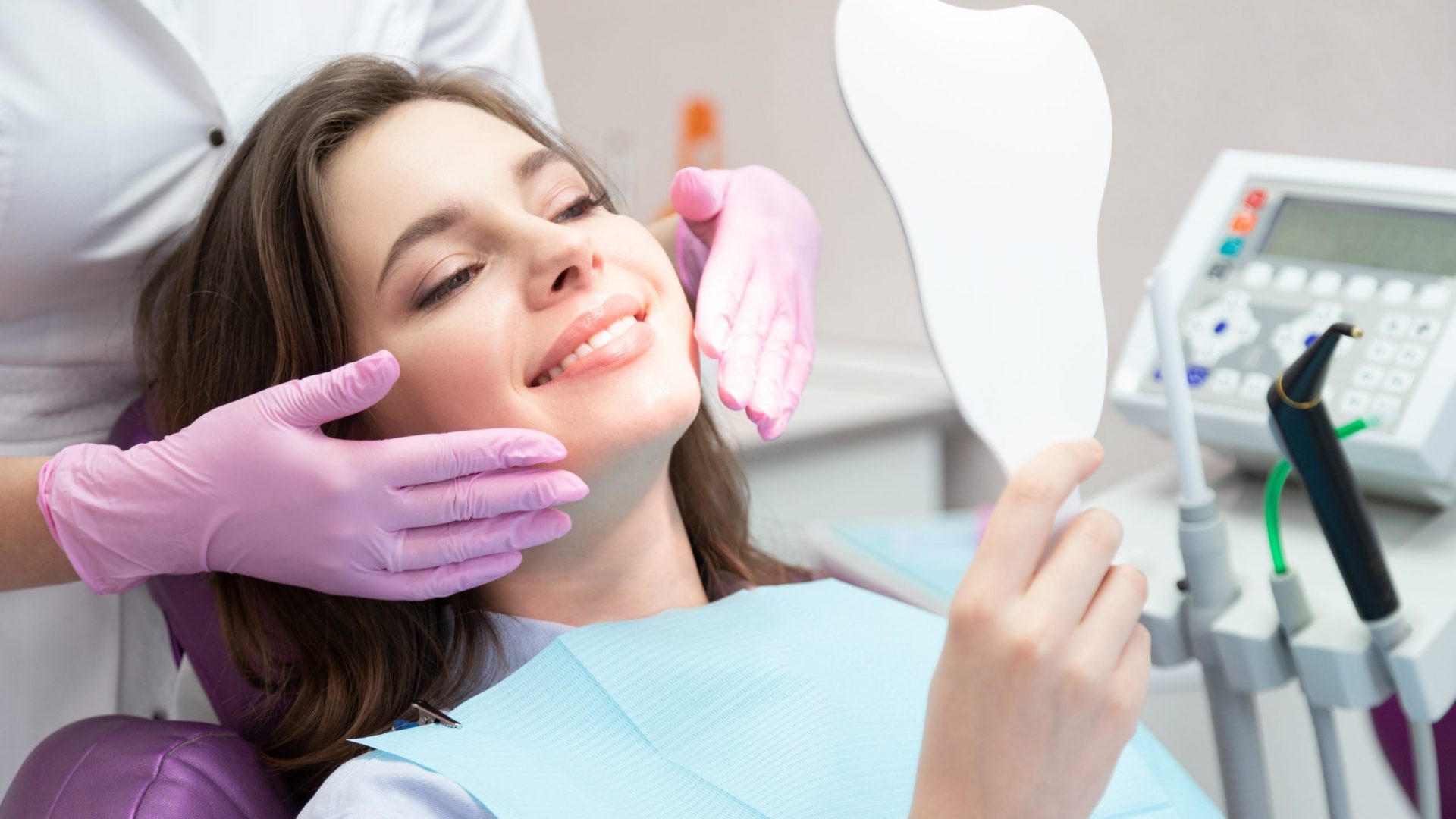 Girl at stomatologist appointment in dental clinic Young glad smiling woman patient looking at mirror after teeth whitening procedure, caries treatment, toothache elimination. Pretty happy girl at stomatologist appointment in dental clinic